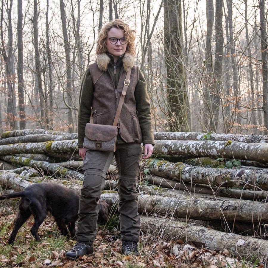 Jägerin mit Filztasche vor Holzstoss im Wald