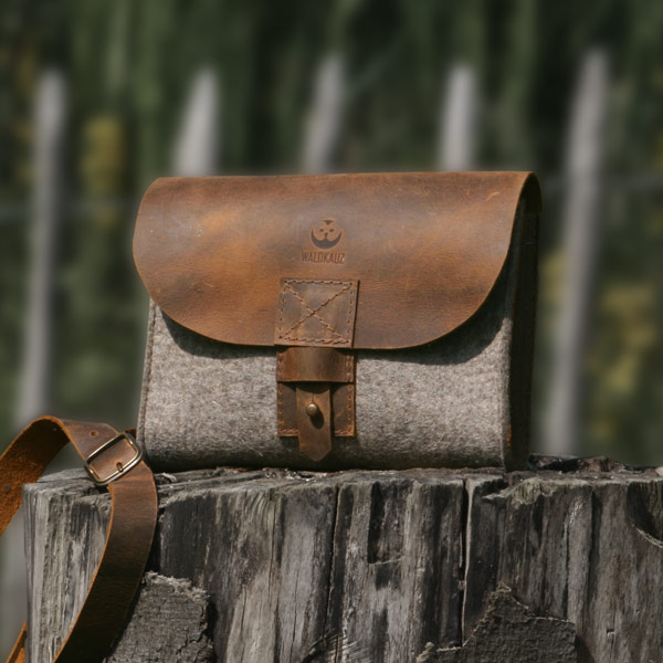Filztasche mit Lederdeckel steht auf Holzpfosten